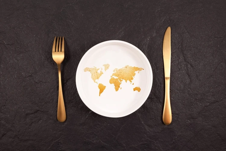 Zu sehen ist mittig ein Teller, in dem die Umrisse der Weltkarte abgebildet sind und Messer und Gabel.